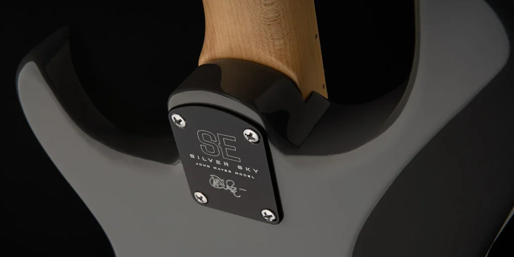 Close-up of the PRS SE Silver Sky electric guitar's neck joint, featuring a black neck plate with "SE Silver Sky John Mayer Model" engraving and John Mayer's signature.